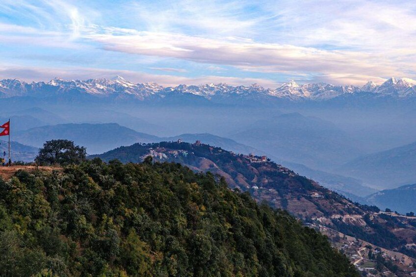 A mountainous landscape with snow-capped peaks, a flag on a hill, and dense forest. 1