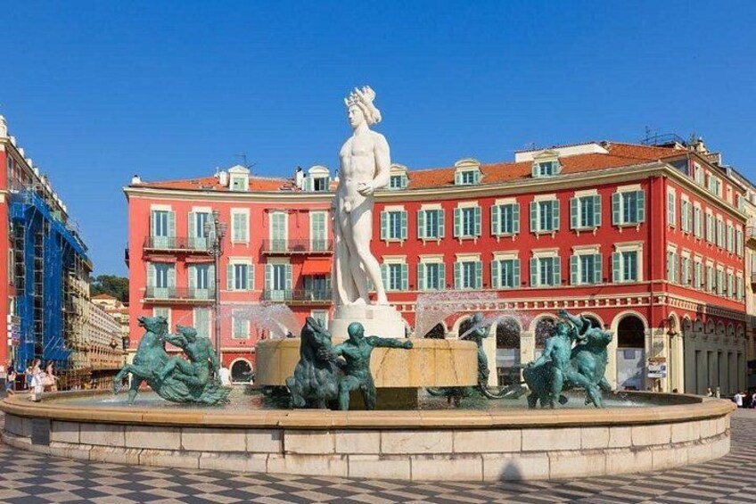 A fountain with statues, a red building with balconies, and a clear blue sky. 1