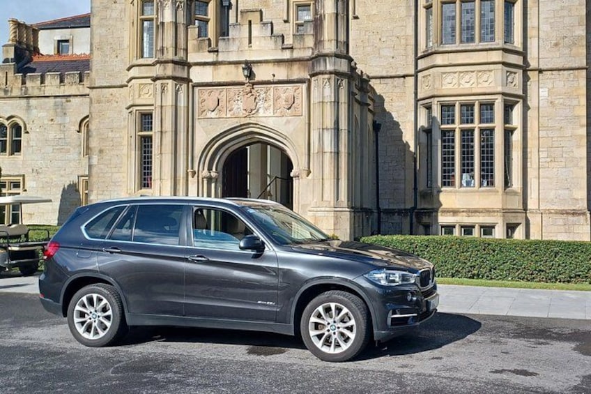 A gray SUV parked in front of a historic building with detailed stonework and arched windows. 2