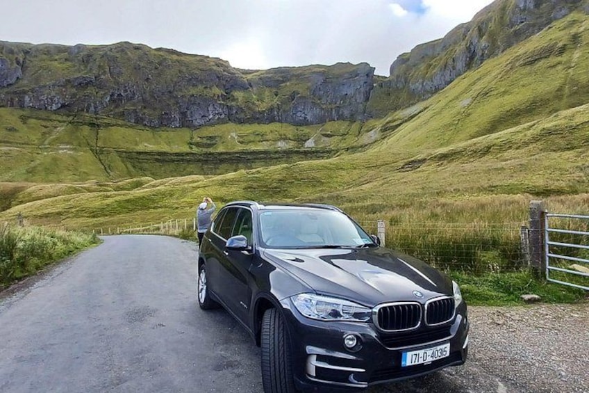 A black BMW parked on a rural road with a person standing in the background. 3