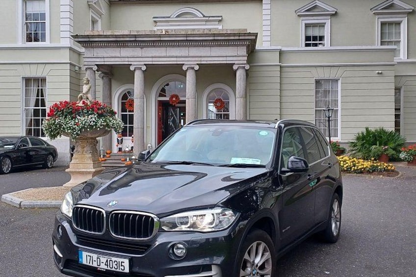 A black BMW SUV parked in front of a building with classical architecture, including columns and a decorative entrance. 4