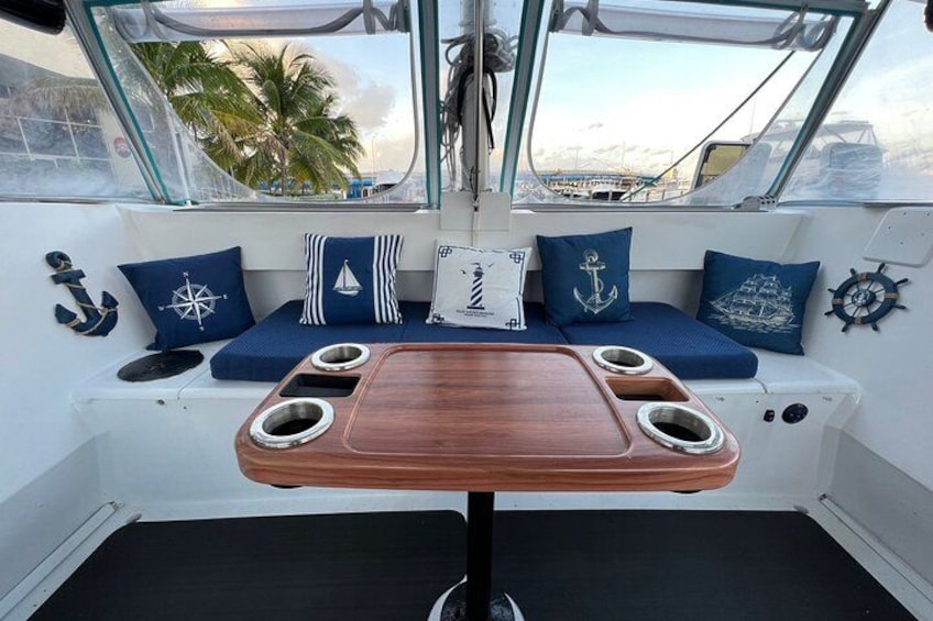 A boat's deck with a wooden table, blue cushions, and nautical-themed pillows. 3