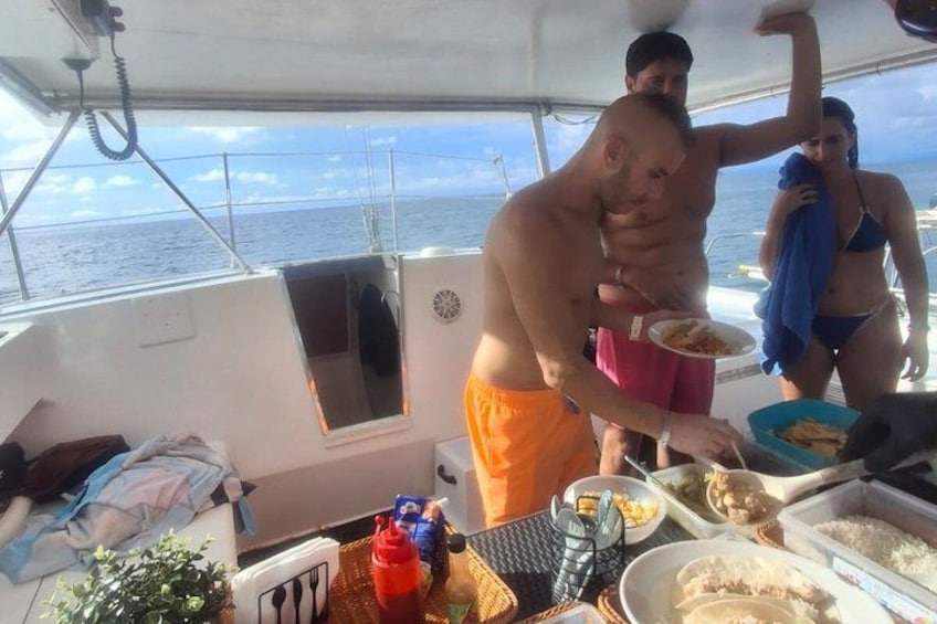 En båd med mennesker, der spiser, en kvinde i bikini og en mand i orange shorts. 4