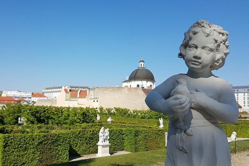 Una estatua de un niño en un jardín, con un edificio de forma abovedada al fondo. 3