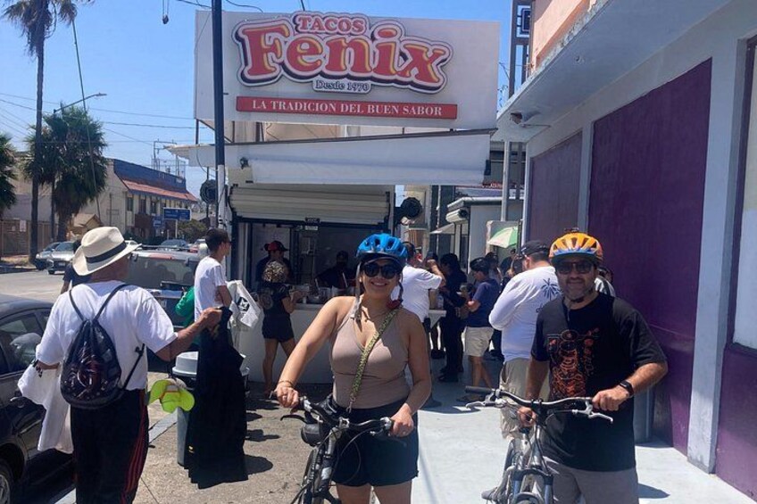 Una calle con un restaurante de tacos, gente caminando y bicicletas. 2