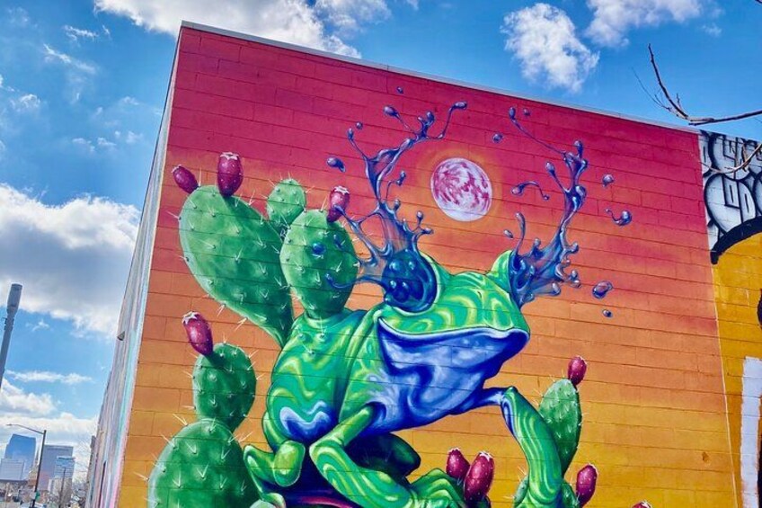 Ein Wandbild zeigt einen Frosch, Kakteen und eine Sonne an einem Gebäude. 4