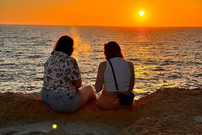 Dos personas sentadas en una playa arenosa, contemplando la puesta de sol sobre el océano. 5