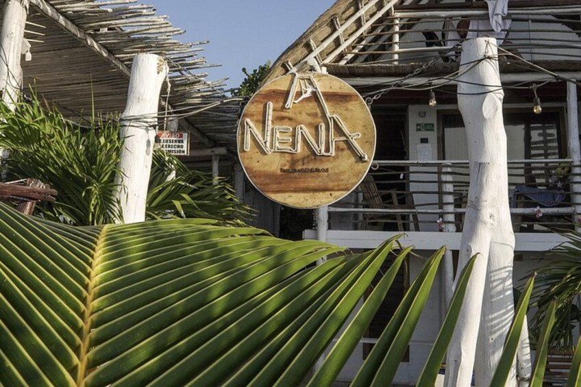 Et træskilt med teksten 'NENA' og en palme i forgrunden. 3