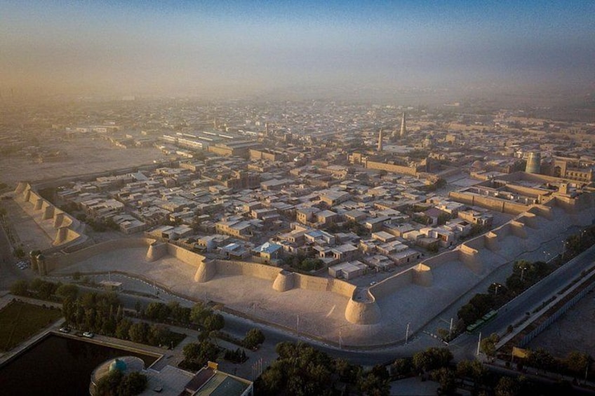 An aerial view of a fortified city with a large central area surrounded by walls, a river, and a bridge. 1