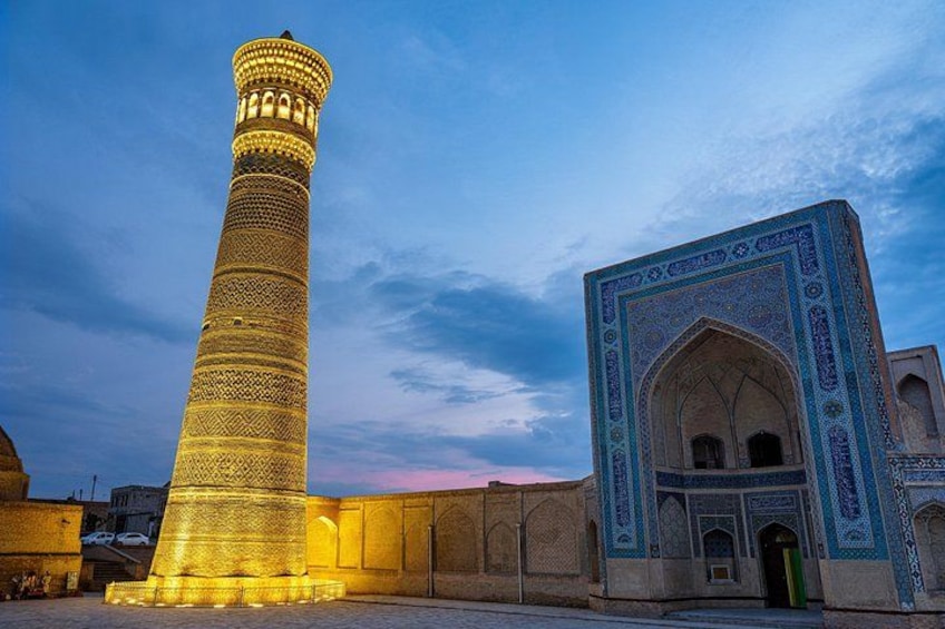 A tall minaret with intricate patterns, a large arched entrance with detailed tile work, and a clear sky. 2
