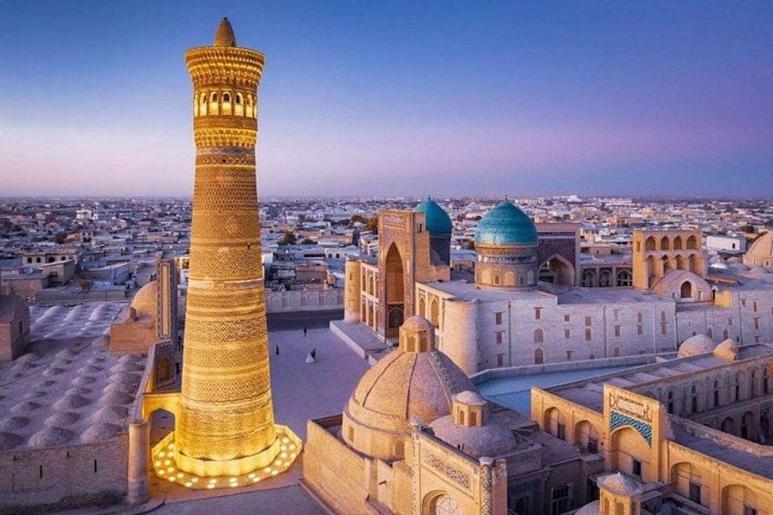A large, illuminated minaret in a historic cityscape with domed buildings. 3