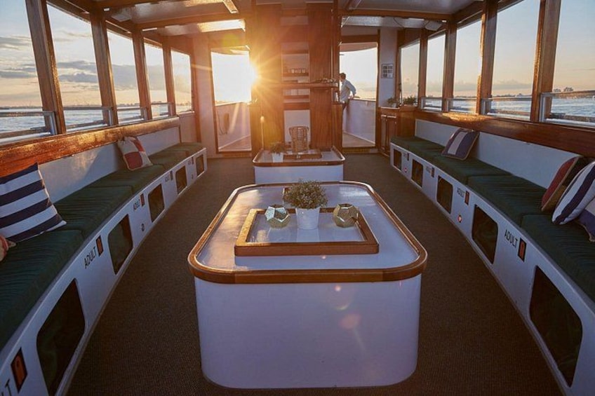 A sunlit interior with a central table, seating along the walls, and a view of the sea. 1