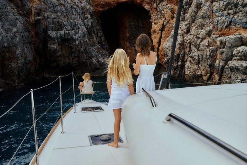 A boat with two people standing at the bow, a rocky coastline, and a cave entrance. 5