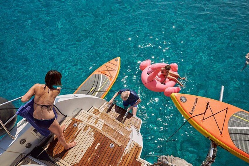 A boat docked in a clear blue water body with inflatable rings and a paddleboard. 4