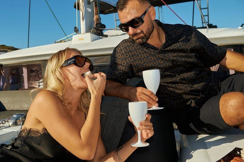 A person holding a white cup, another person sitting beside them, and a boat in the background. 3