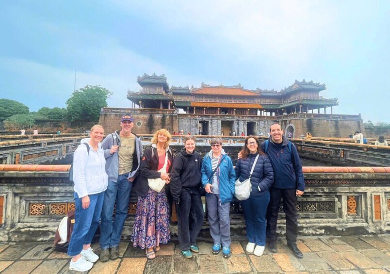 Eine Gruppe von Menschen steht vor einem traditionellen chinesischen Gebäude mit einem schiefergedeckten Dach und aufwendiger Architektur. 3