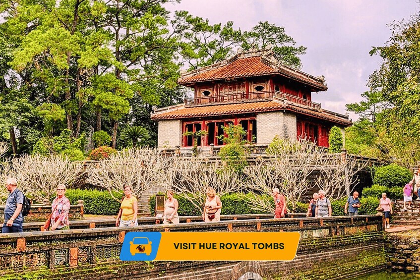 Ein traditionelles chinesisches Gebäude mit rotem Dach und hölzernen Balkonen, umgeben von üppigem Grün und einer Steinbrücke, auf der Menschen unterwegs sind. 5