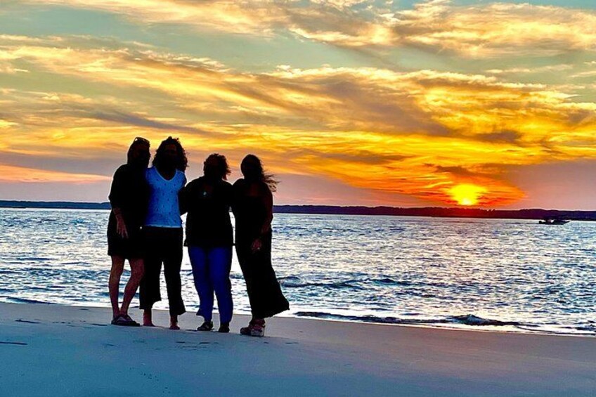 A sunset over a beach with four silhouetted figures standing together. 3