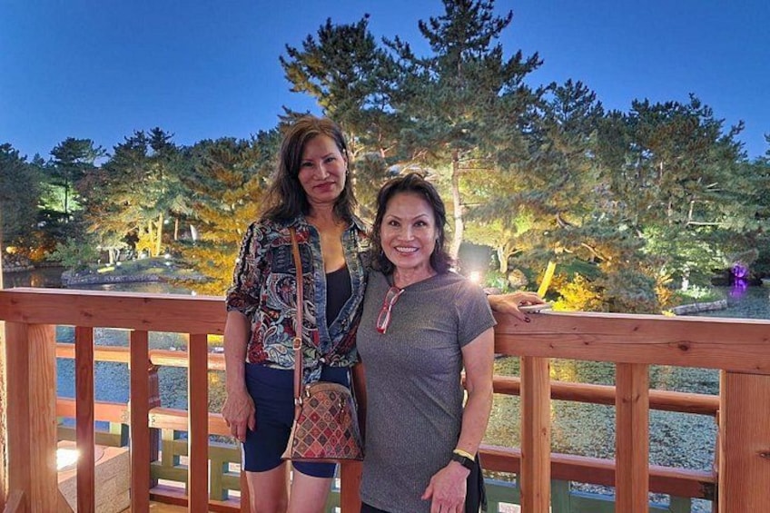Two people standing on a wooden deck with a garden and trees in the background. 5