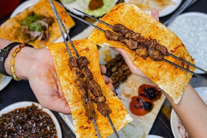 A person holding a skewer of meat on a flatbread. 1