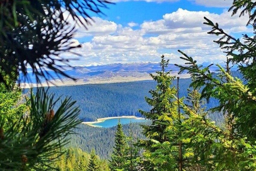 A mountainous landscape with a lake surrounded by dense forest and distant mountains. 1