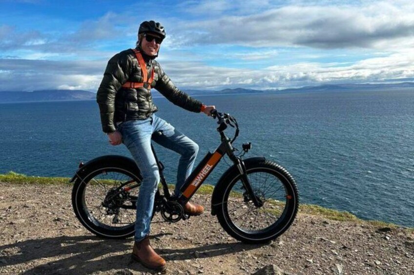 A person riding a mountain bike on a rocky path with a scenic view of the ocean and mountains in the background. 2
