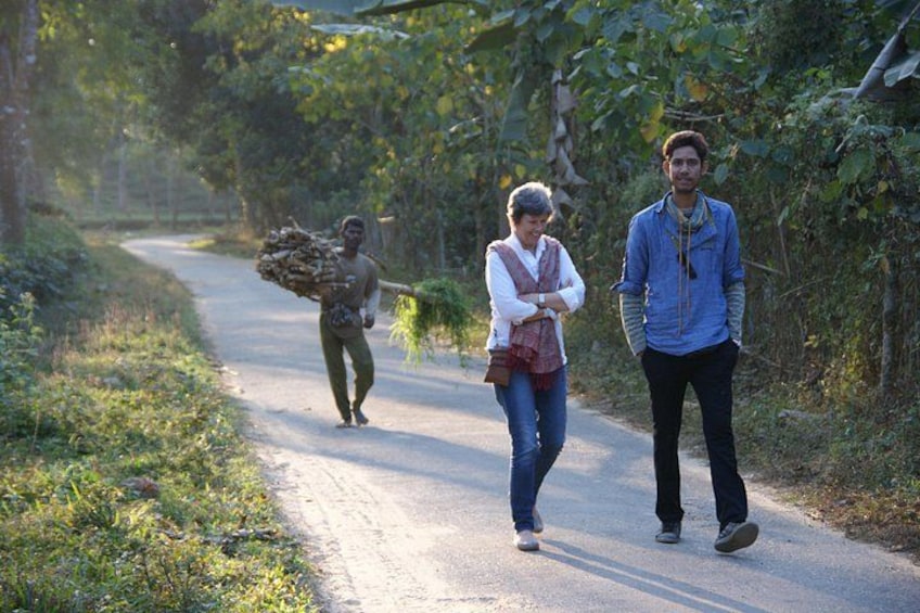 A rural road with a person carrying firewood and two people walking. 1