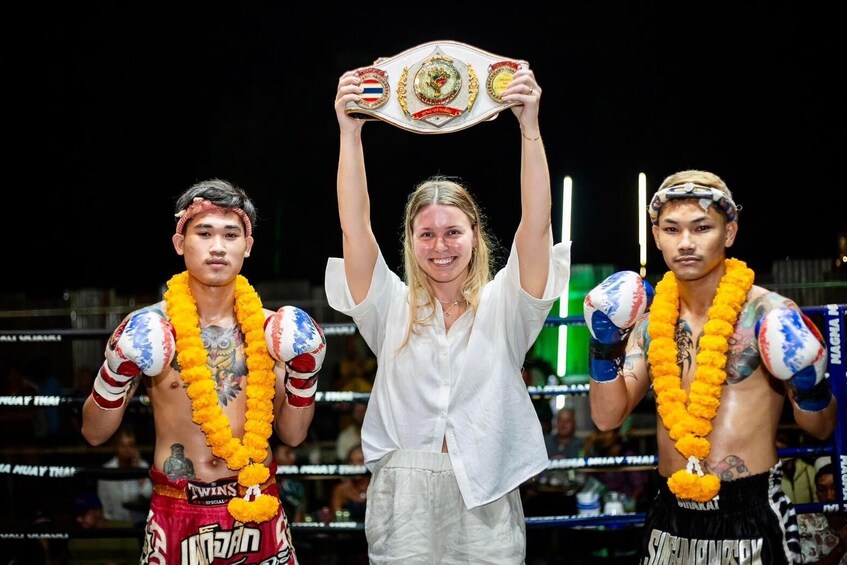 Tres personas en un ring de boxeo, una sosteniendo un cinturón de campeonato. 1