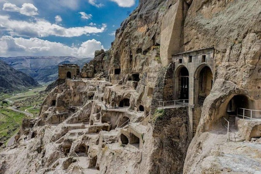 A rugged mountainous landscape with ancient rock-cut architecture, including a series of arches and a small tower. 2