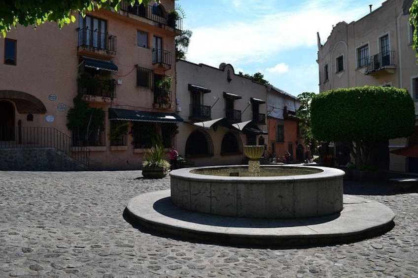 A cobblestone square with a circular fountain, surrounded by buildings with balconies and arched windows. 1