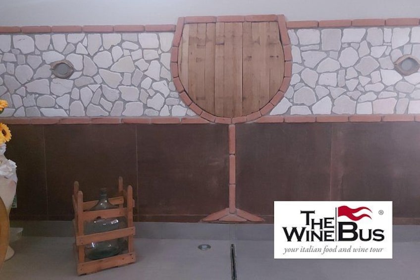 A wine tasting area with a stone wall, a wooden wine rack, and a logo for 'The Wine Bus' tour. 5