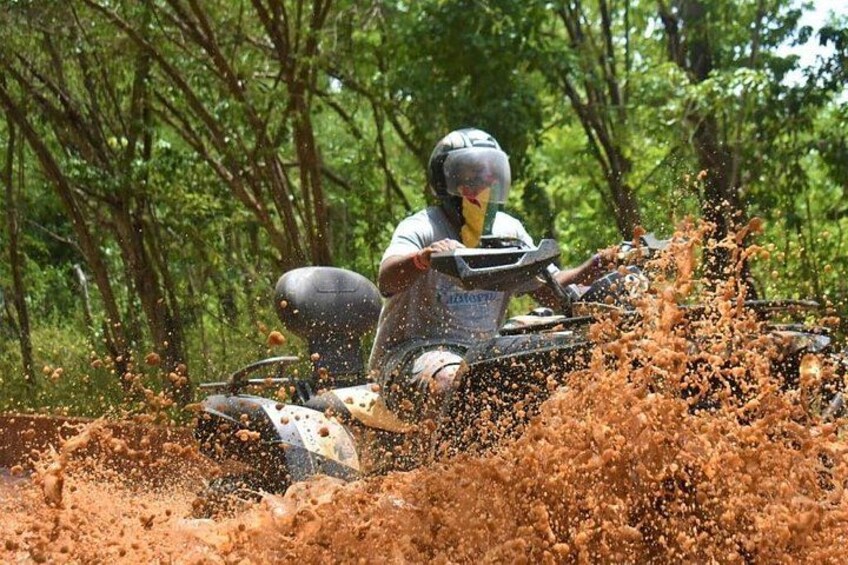 Iemand rijdt op een quad door een modderig gebied, met modder spatten rondom. 2