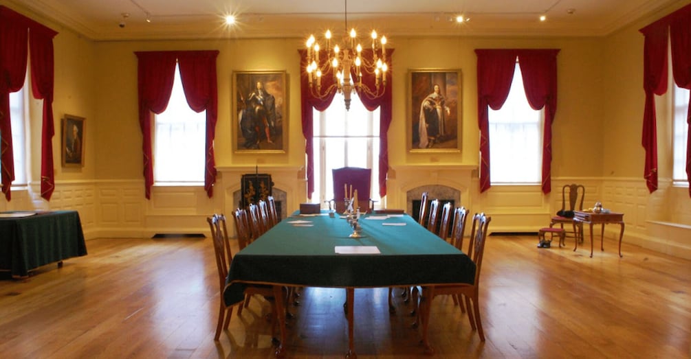 Una sala de reuniones formal con una larga mesa, sillas, una araña y dos grandes cuadros en las paredes. 4