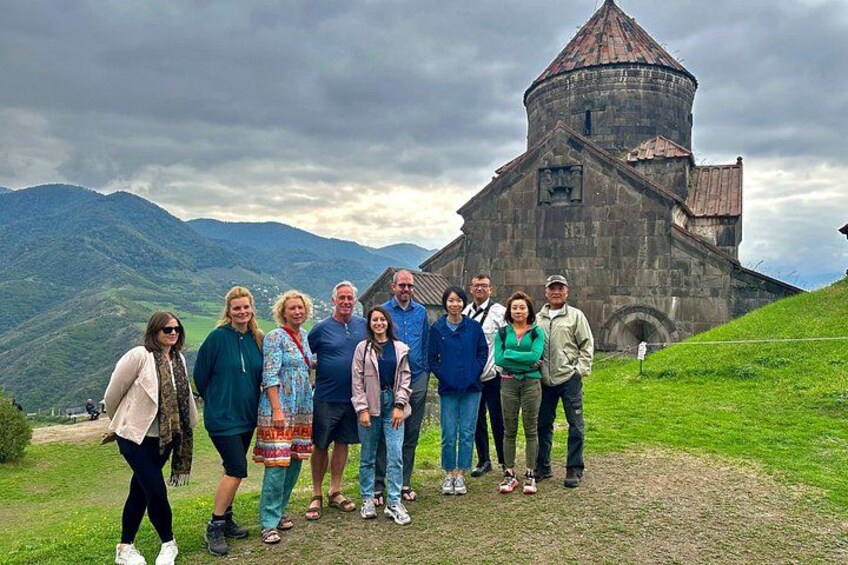 A group of people standing in front of a historic building with a dome, surrounded by a mountainous landscape. 1