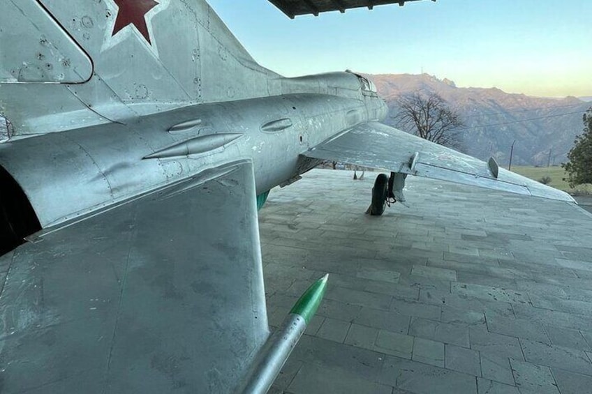 A military aircraft with a red star insignia, a green missile, and a mountainous landscape in the background. 5