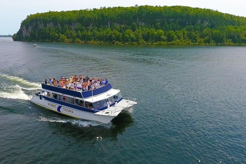 A boat with 'SCENIC TOURS' written on it, surrounded by water and a forested island in the background. 2