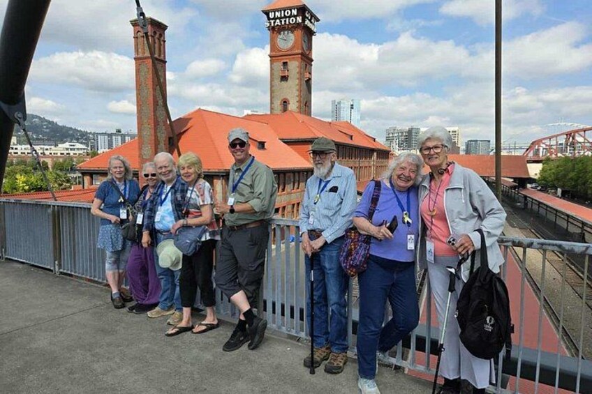 A group of people standing on a bridge with a clock tower and a red-roofed building in the background. 2