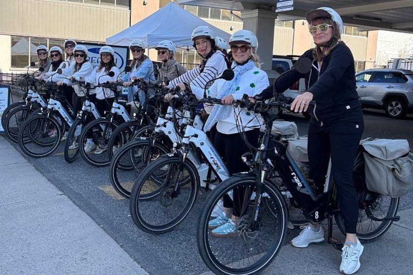 A group of people with bicycles, some wearing helmets, standing in a line on a sidewalk. 4