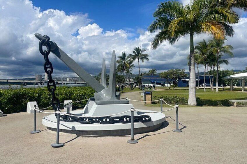 A naval cannon on display, surrounded by a circular fence, with palm trees and a clear sky in the background. 3