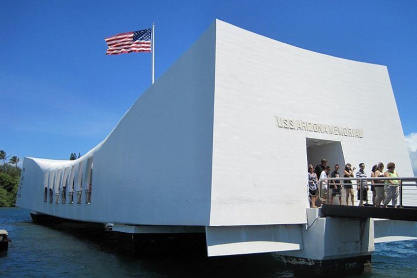 A white building with the USS Arizona Memorial on a body of water. 1