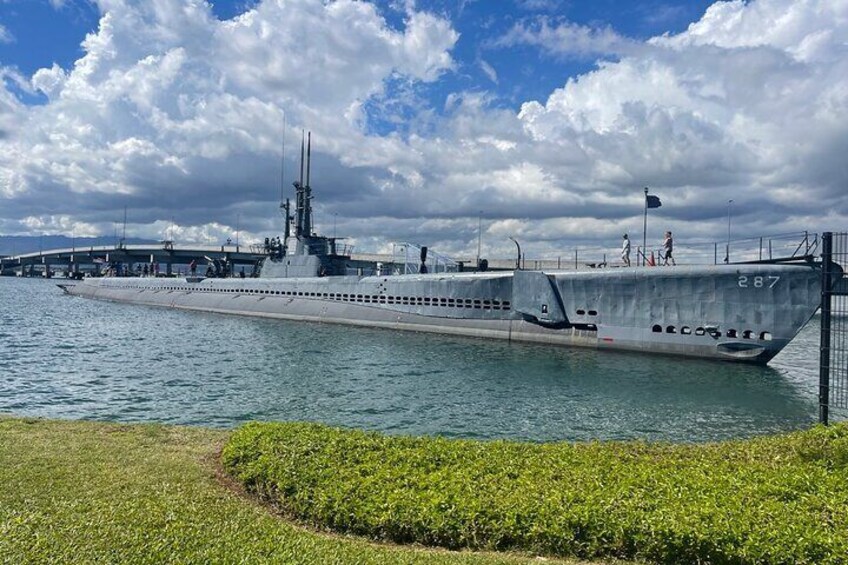 A large naval ship docked at a pier with a grassy area in the foreground. 2