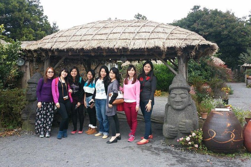 A group of people standing under a thatched structure in a garden with stone sculptures and a large pot. 3