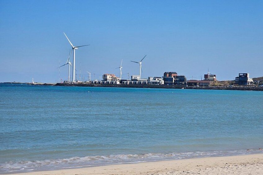 A coastal area with wind turbines, a sandy beach, and buildings. 2