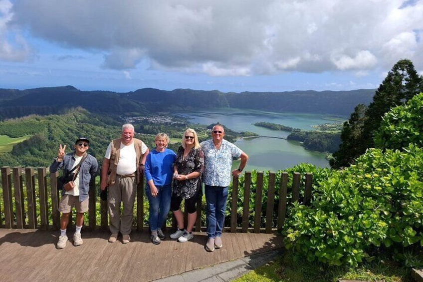 Un grupo de personas de pie sobre una plataforma de madera con una vista panorámica de un lago y montañas al fondo. 5