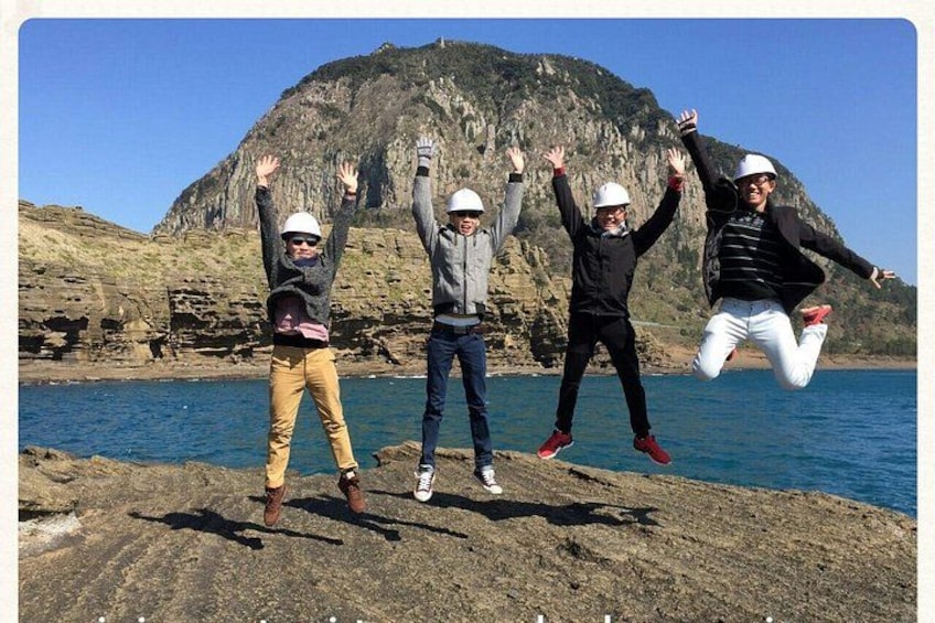 Three people jumping in front of a rocky coastline with a mountain in the background. 1