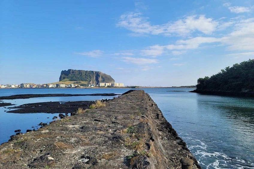 A rocky pier extending into calm waters, a distant hill with a flat top, and a clear blue sky. 3