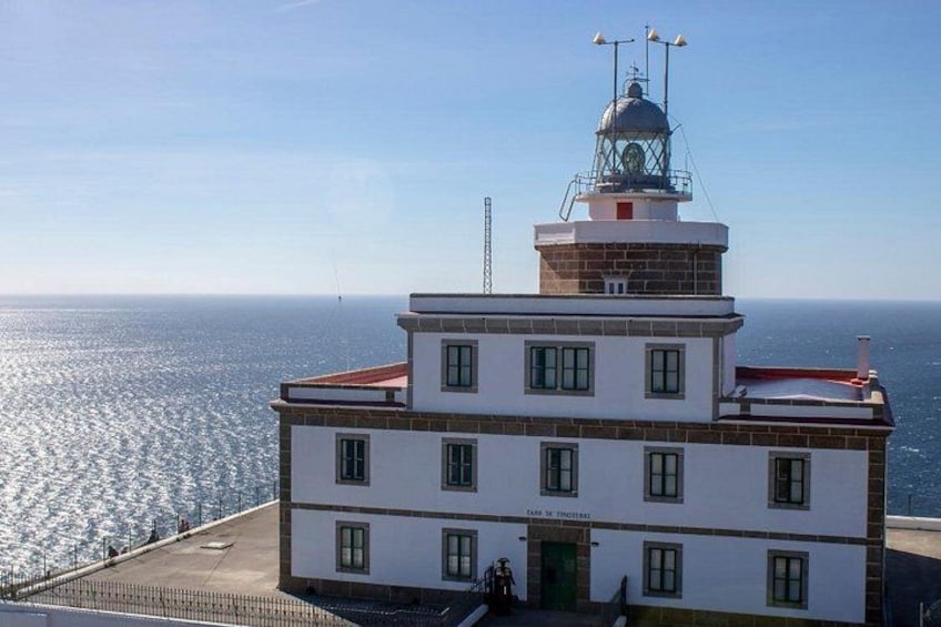 A lighthouse with a white and brown structure, a clear sky, and the ocean in the background. 1