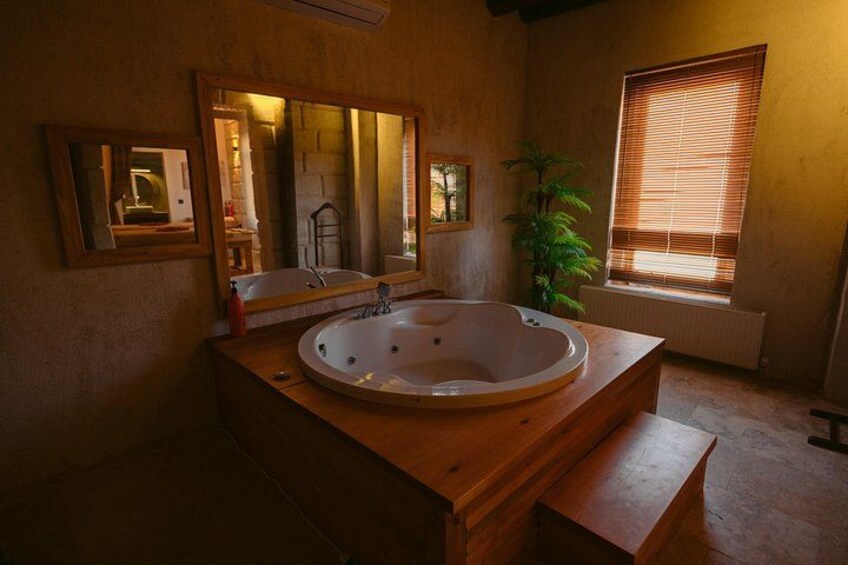 A bathroom with a wooden vanity, a large bathtub, a mirror, and a window with blinds. 5
