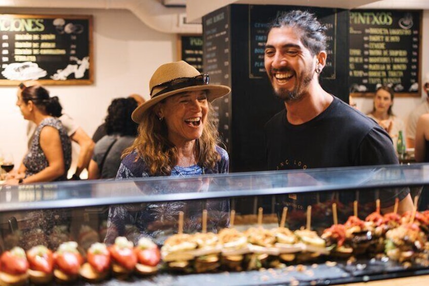 A person wearing a hat and a black shirt standing in front of a food display with various fruits and vegetables. 1