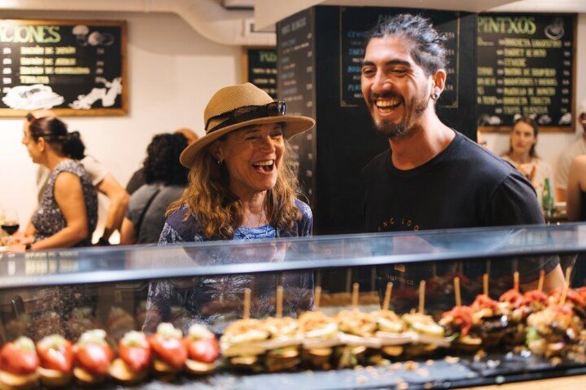 Une personne portant un chapeau et un t-shirt noir, debout devant un présentoir où sont exposés divers fruits et légumes. 1